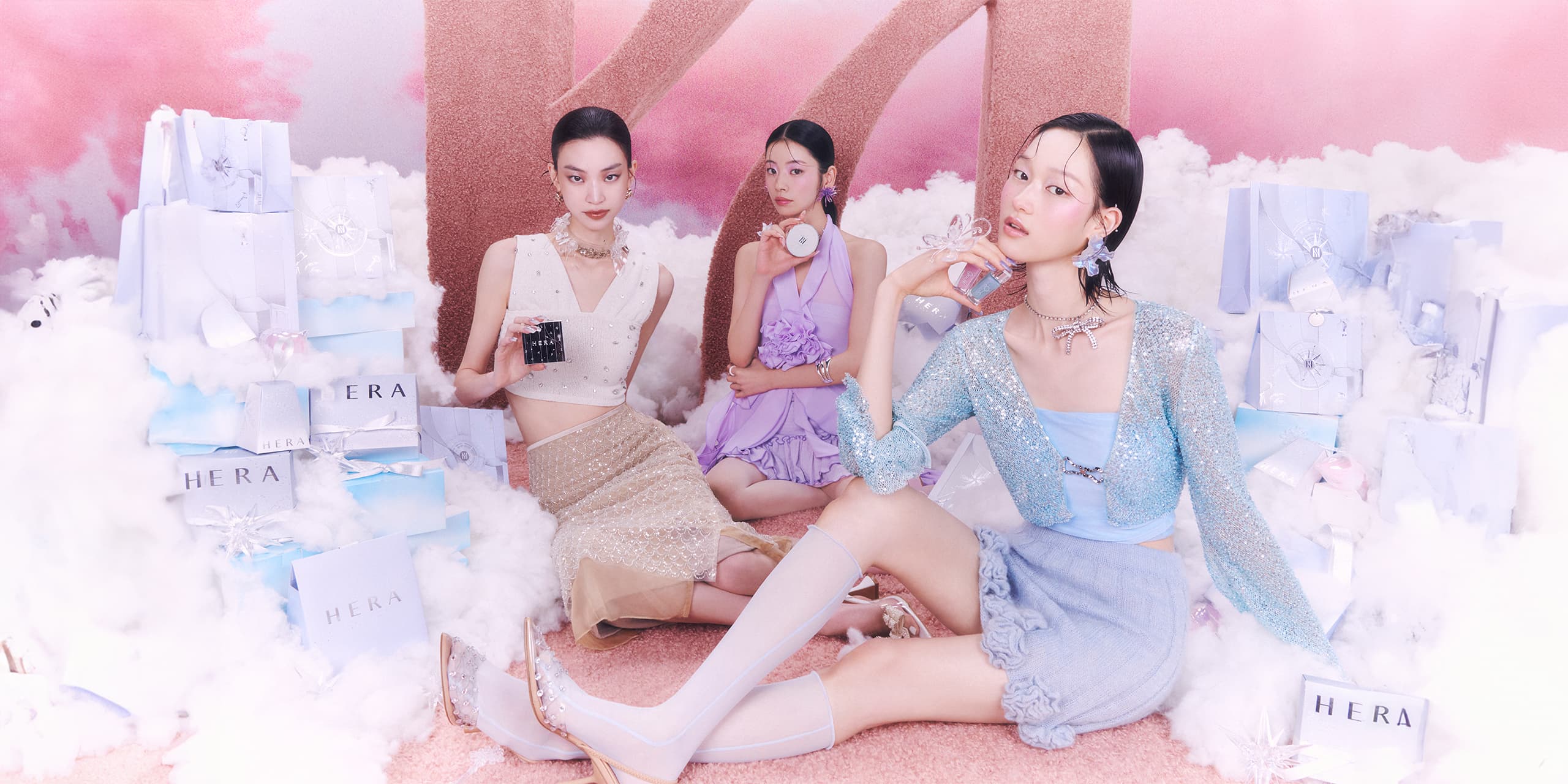 Three models holding HERA HOLIDAY QUAD EYE COLOR DREAMSCAPE VOYAGE, SENSUAL HOLIDAY LIP OIL LAVENDER SHOWER, CLOUD NINE, HOLIDAY CUSHION CASE