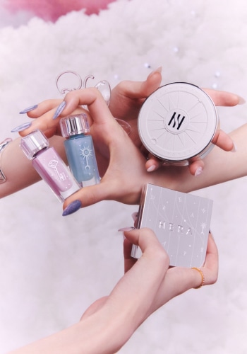 Models holding HERA HOLIDAY QUAD EYE COLOR DREAMSCAPE VOYAGE, SENSUAL HOLIDAY LIP OIL LAVENDER SHOWER, CLOUD NINE, HOLIDAY CUSHION CASE